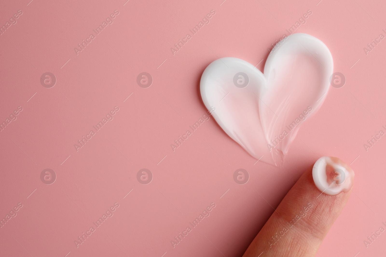 Photo of Woman holding sample of facial cream on pink background, top view