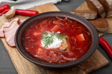 Photo of Tasty borscht with sour cream in bowl served on grey wooden table, closeup