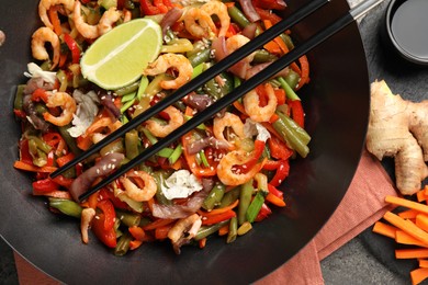 Shrimp stir fry with vegetables in wok and chopsticks on grey table