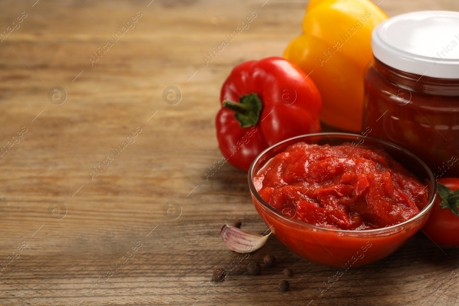 Photo of Delicious lecho, fresh vegetables and peppercorns on wooden table. Space for text