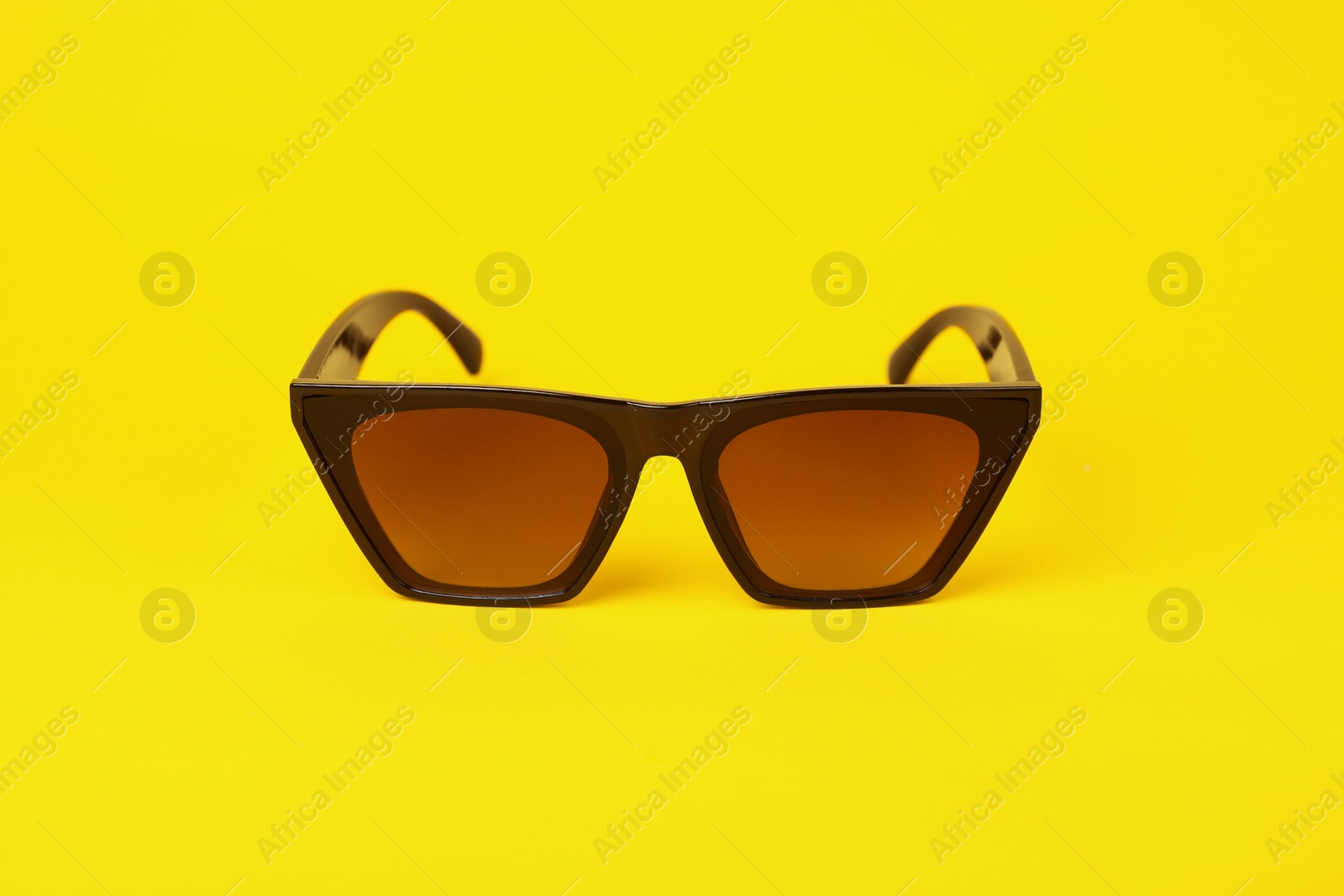 Photo of Stylish pair of sunglasses on yellow background
