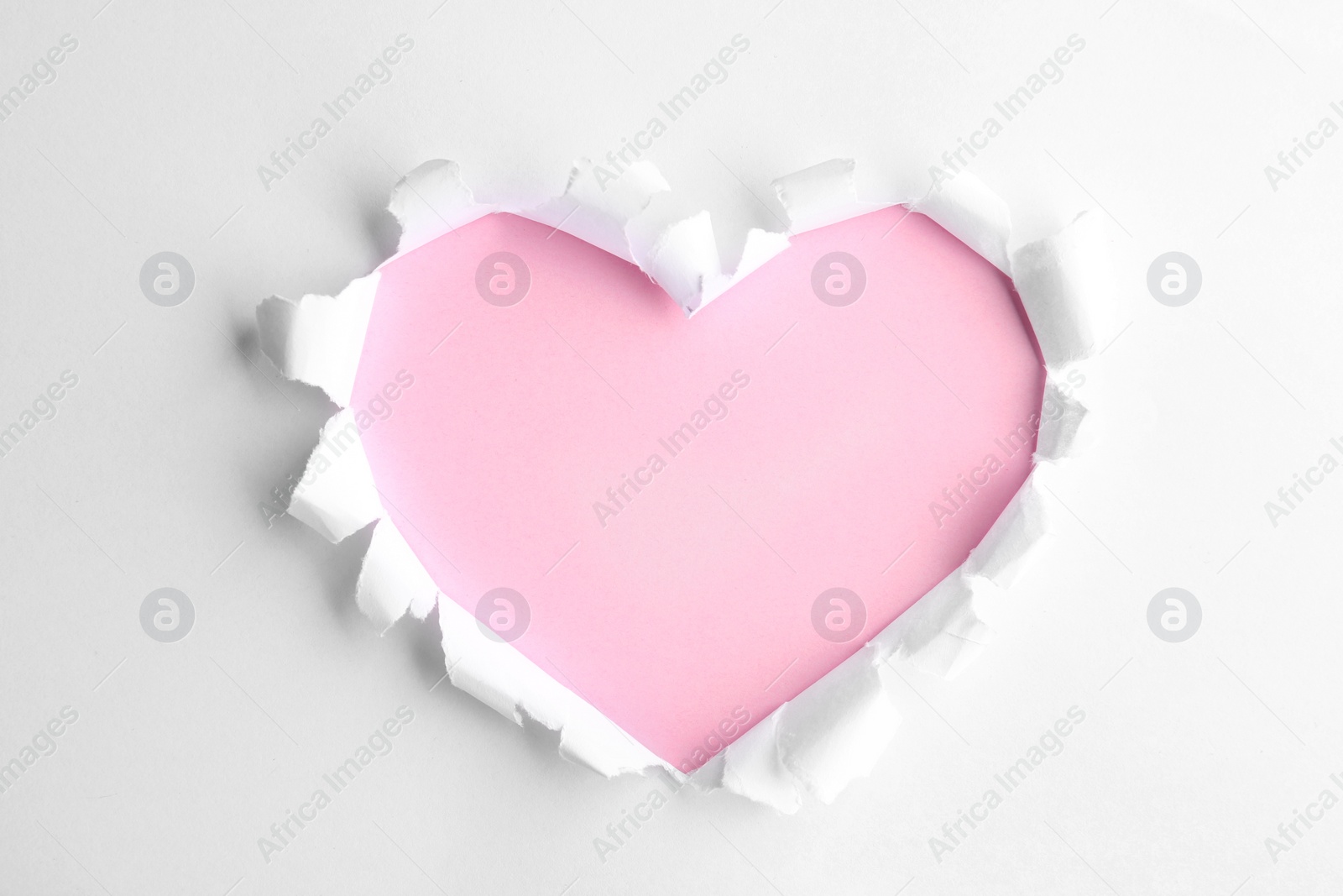 Photo of Torn heart shaped hole in white paper, top view. Pink space for text