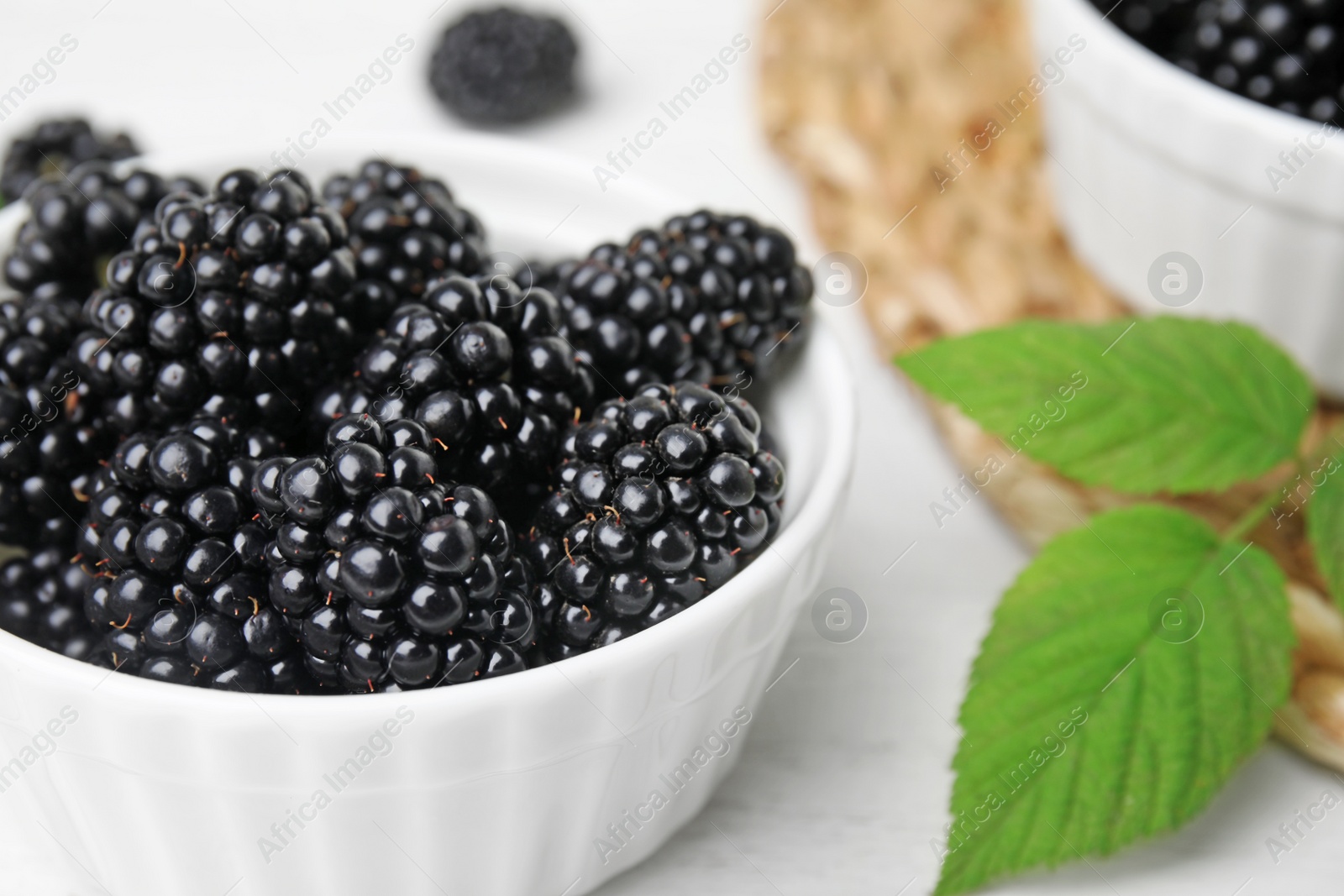 Photo of Bowl of tasty blackberries with leaves on white wooden table, closeup