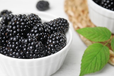 Photo of Bowl of tasty blackberries with leaves on white wooden table, closeup