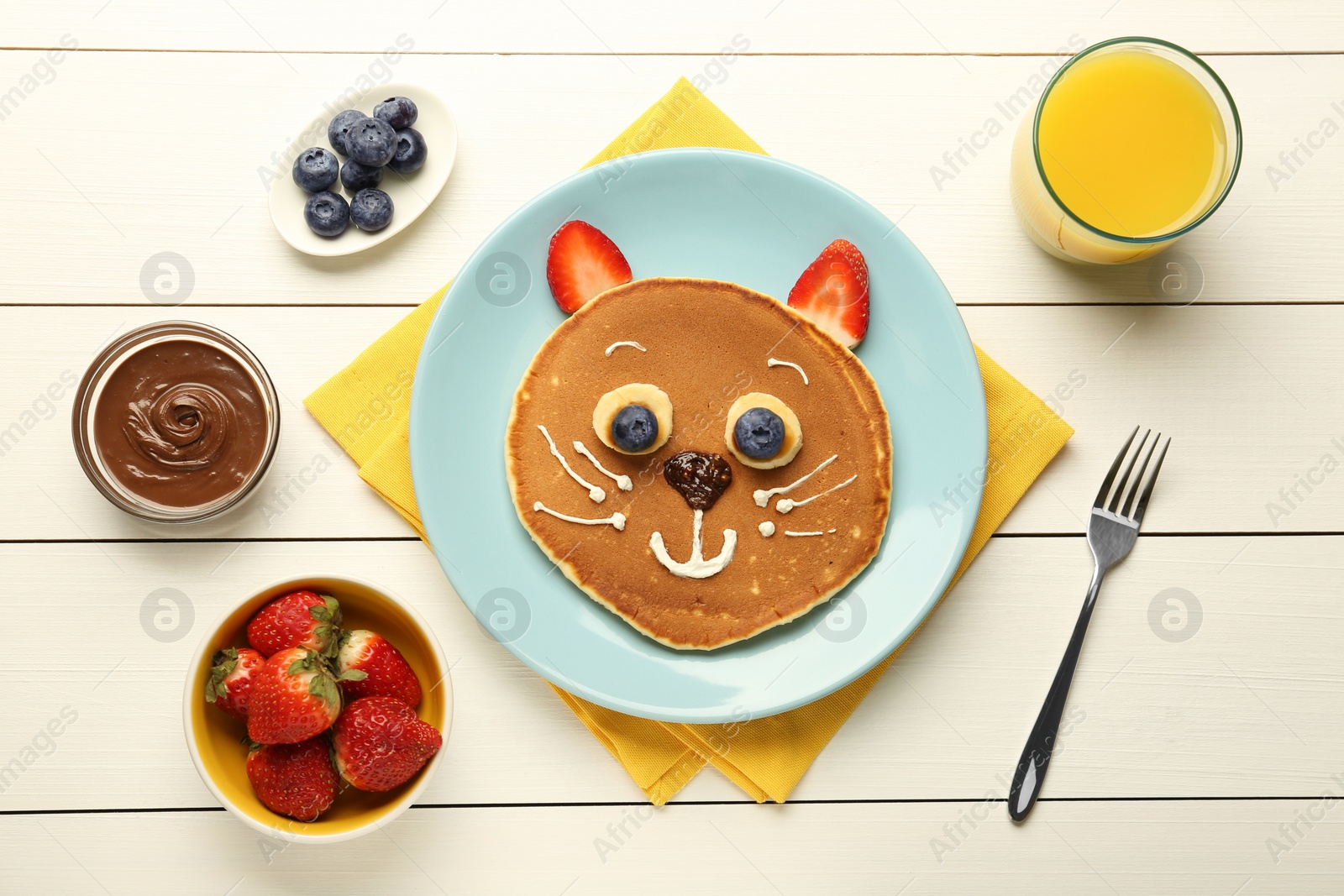 Photo of Creative serving for kids. Plate with cute cat made of pancakes, berries, cream, banana and chocolate paste on white wooden table, flat lay