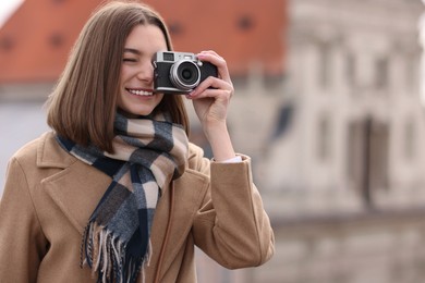 Beautiful woman in warm scarf taking picture with vintage camera outdoors, space for text
