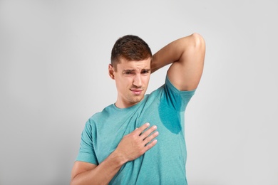 Young man with sweat stain on his clothes against light background. Using deodorant