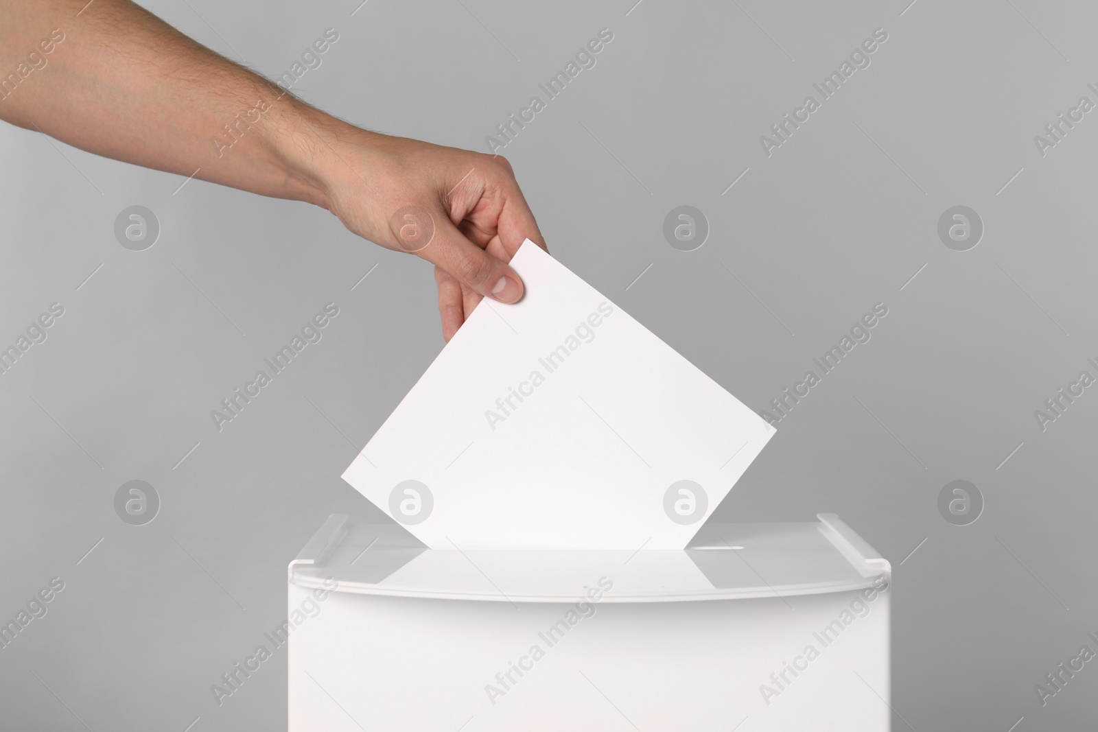 Photo of Man putting his vote into ballot box on light grey background, closeup