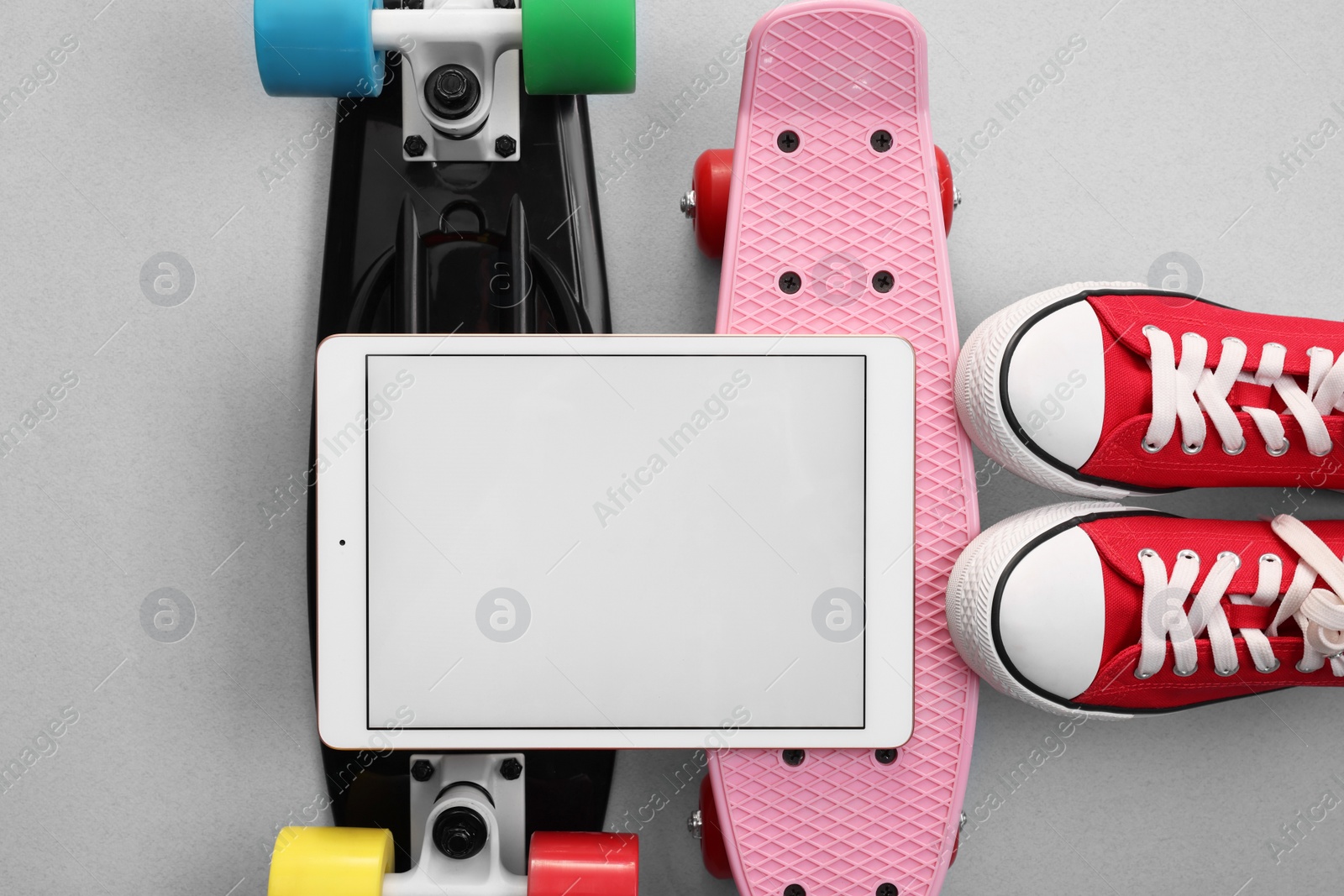 Photo of Modern tablet, skateboards and shoes on light grey background, flat lay. Space for text