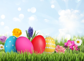 Image of Bright Easter eggs and spring flowers on green grass outdoors