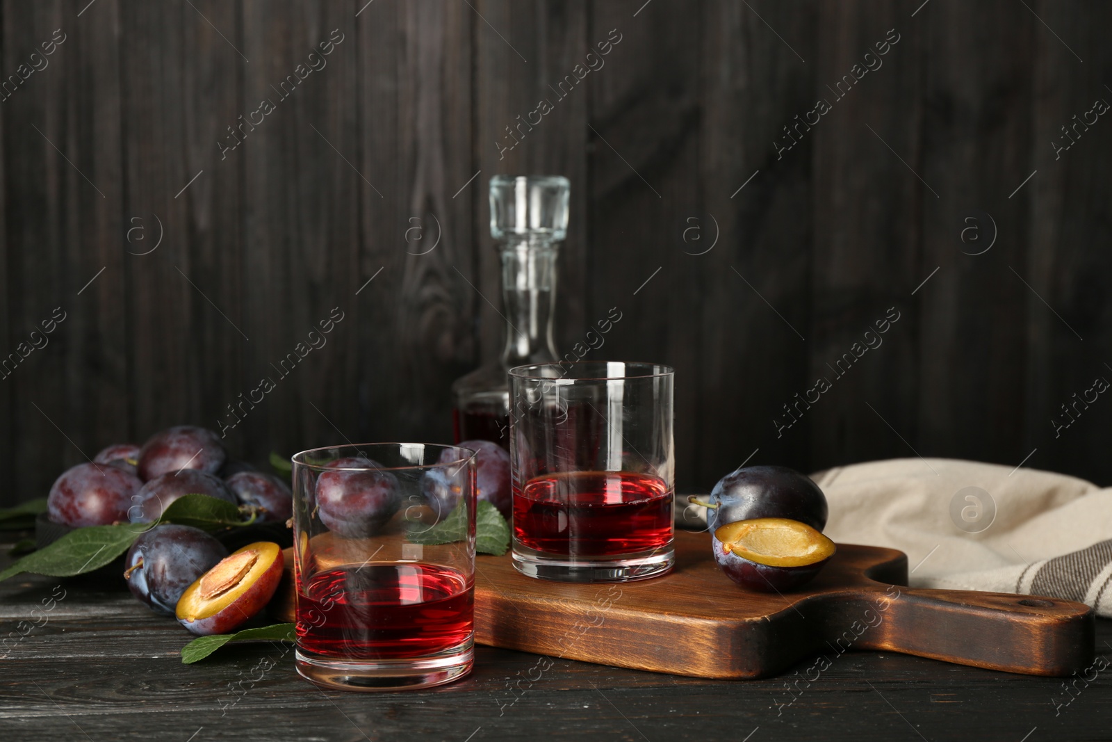 Photo of Delicious plum liquor and ripe fruits on black wooden table. Homemade strong alcoholic beverage