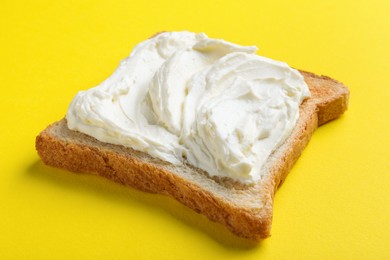 Photo of Slice of bread with tasty cream cheese on yellow background, closeup