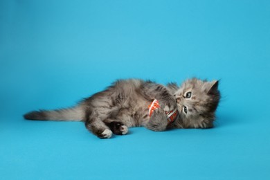 Photo of Cute kitten playing with ball on light blue background. Space for text