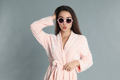 Young woman in bathrobe and sunglasses on grey background