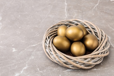 Photo of Golden eggs in nest on color background, space for text