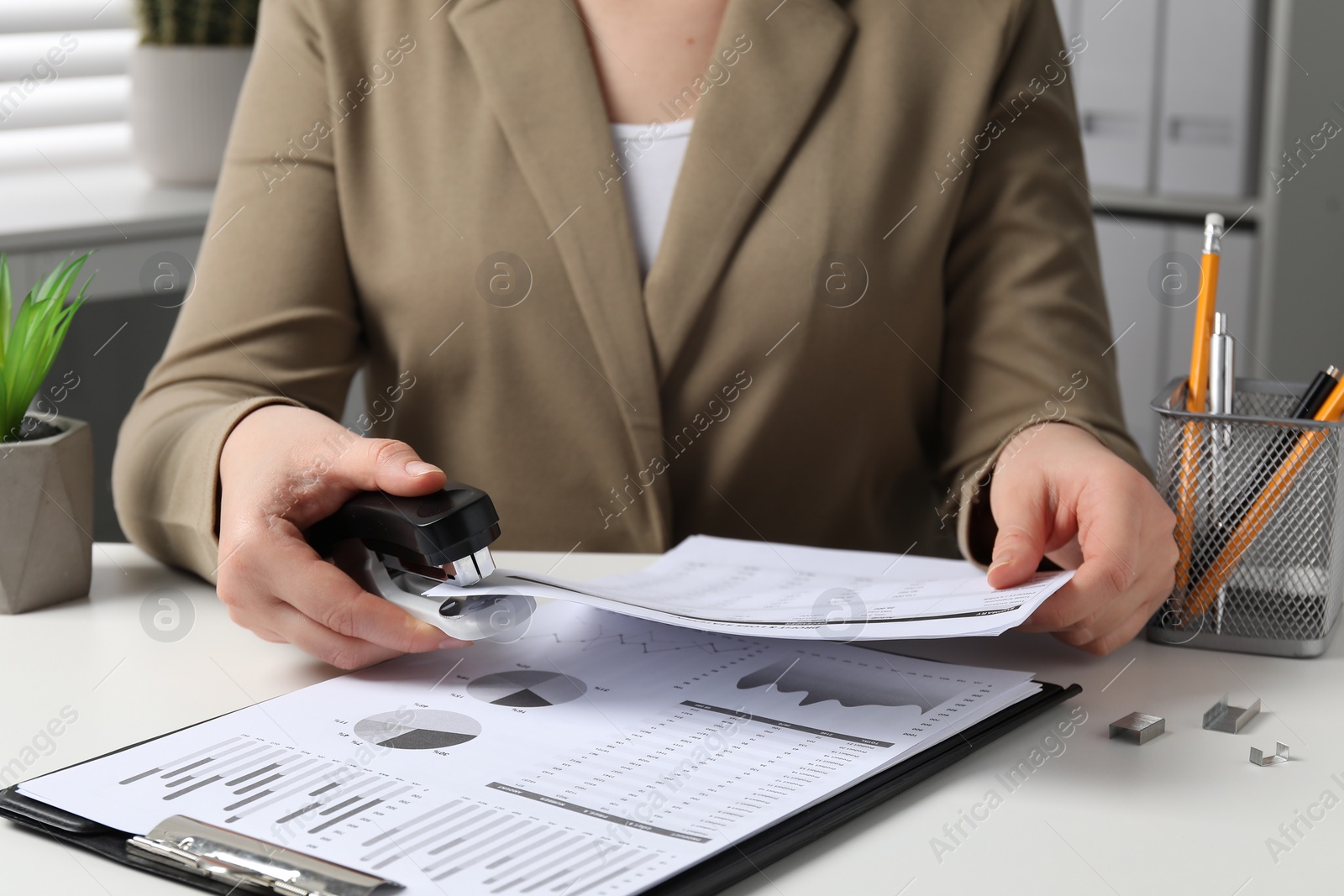 Photo of Woman stapling documents at white table indoors, closeup