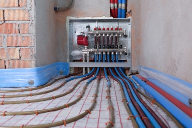 Photo of Underfloor heating system. Manifold with pipes in building