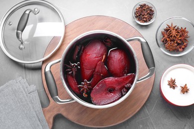 Tasty red wine poached pears and spices in pot on grey table, flat lay