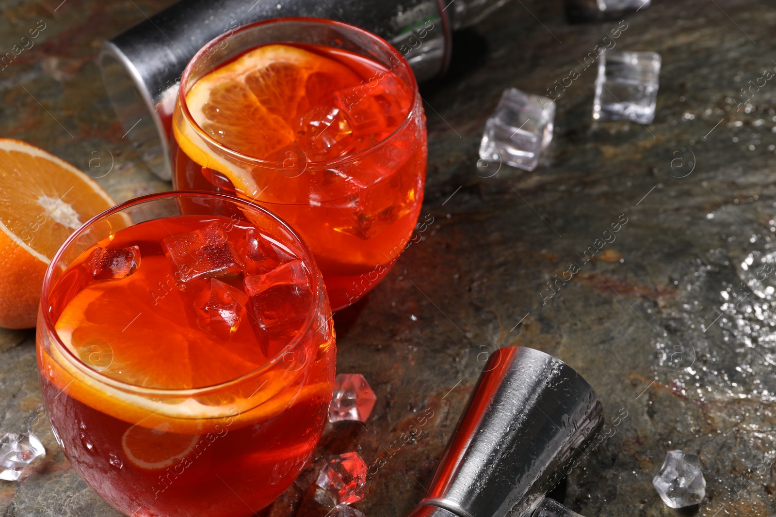 Photo of Aperol spritz cocktail, ice cubes and orange slices in glasses on grey textured table, closeup. Space for text