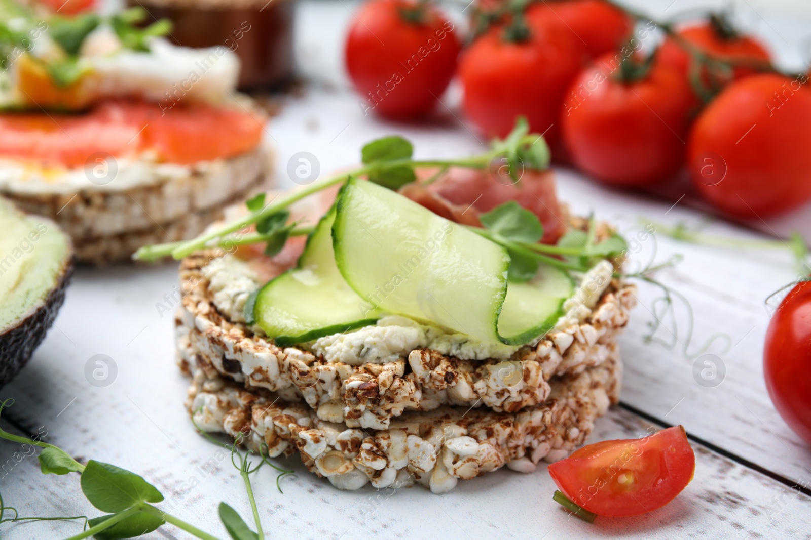 Photo of Crunchy buckwheat cakes with cream cheese, prosciutto and cucumber slice on white wooden table, closeup