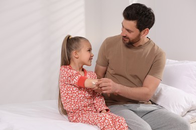 Photo of Father applying ointment onto his daughter's elbow on bed indoors
