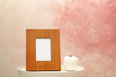 Photo of Blank frame and decorative apple figure on table near color wall. Mock up for design