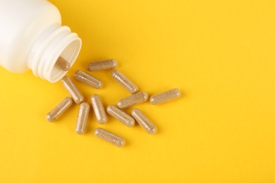 Photo of White medical bottle and vitamin capsules on yellow background, top view. Space for text