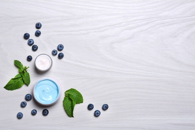 Flat lay composition with jars of body cream on light wooden background. Space for text