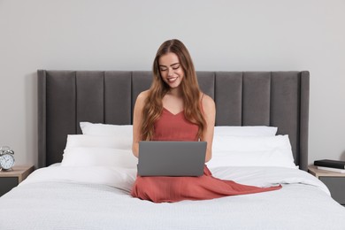 Happy woman with laptop on bed in bedroom