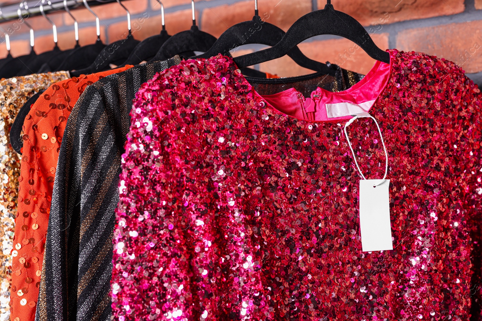 Photo of Preparing for party. Collection of fashionable dresses on hangers near brick wall in showroom, closeup