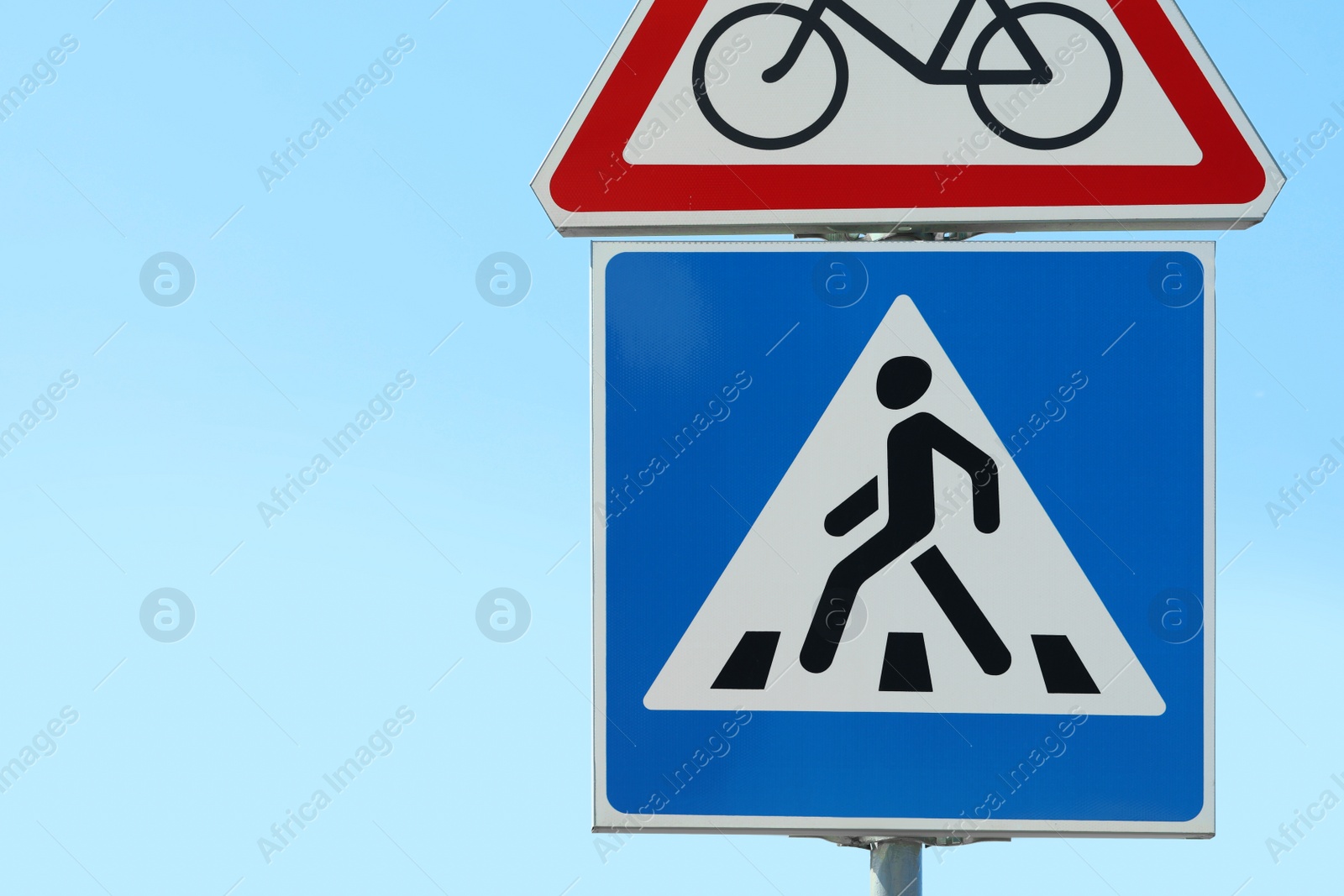 Photo of Post with Pedestrian Crossing and No Bikes traffic signs against blue sky on sunny day