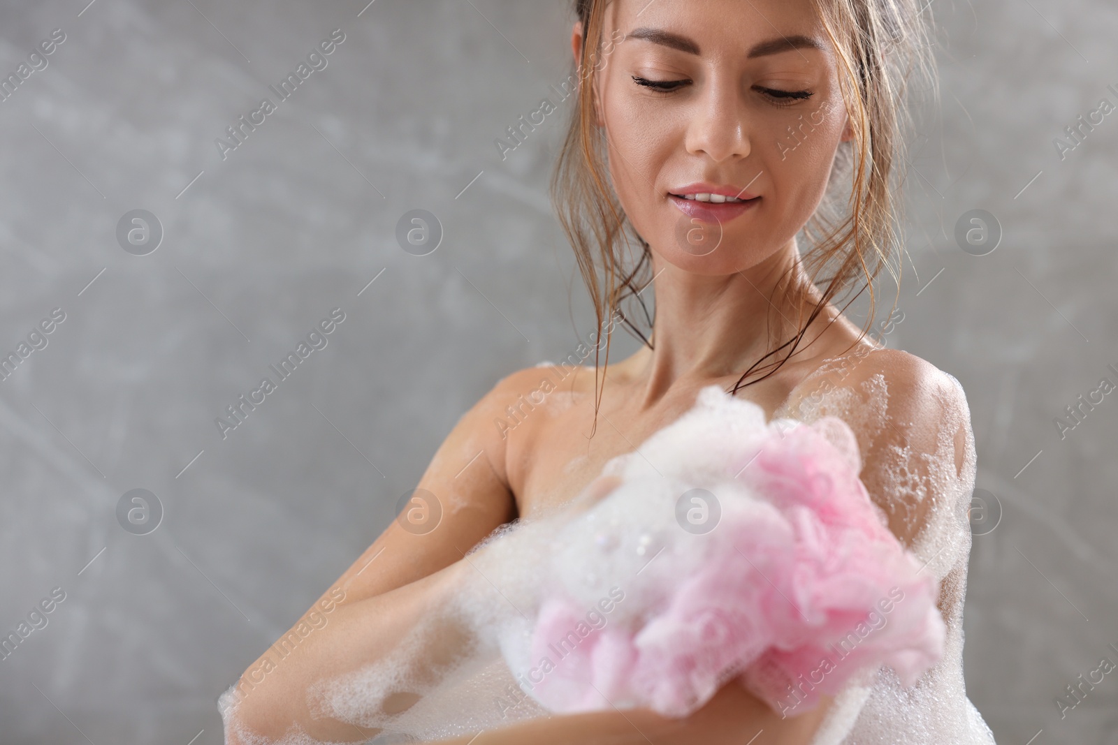 Photo of Beautiful woman with mesh pouf taking shower indoors, space for text