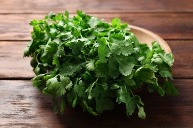 Photo of Fresh coriander in bowl on wooden table, closeup