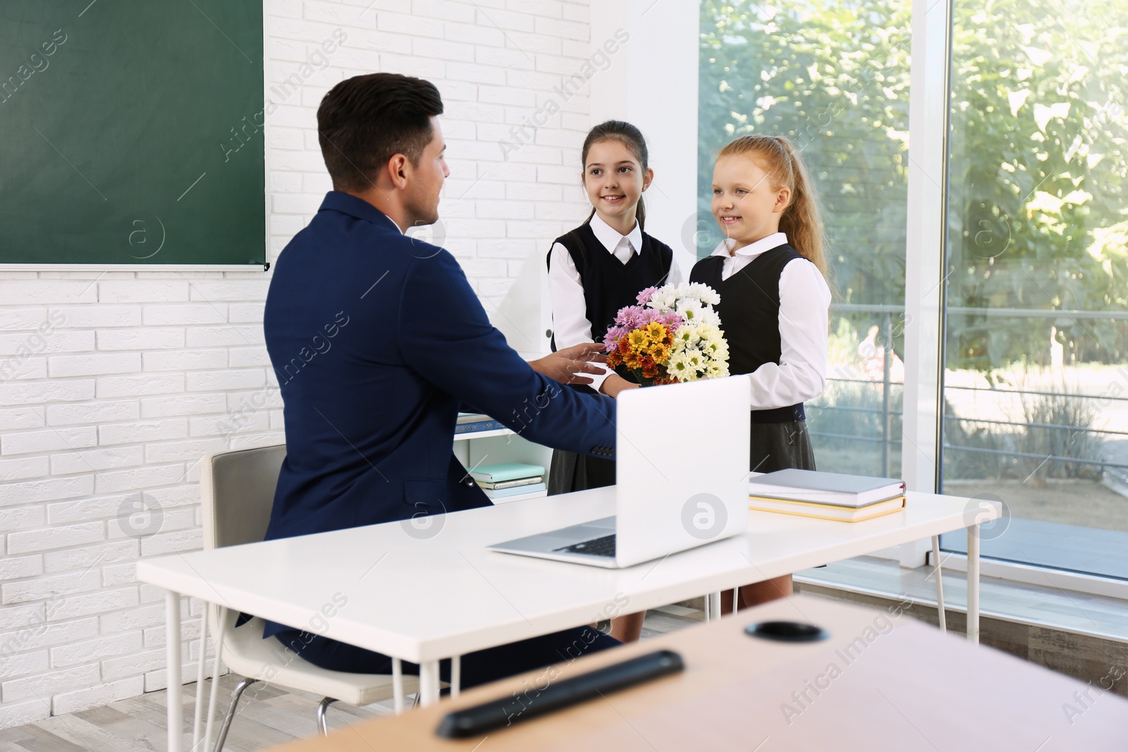 Photo of Schoolgirls congratulating their pedagogue with bouquet in classroom. Teacher's day