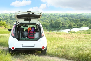 Photo of Car with camping equipment in trunk on green field. Space for text