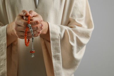 Muslim man with misbaha praying on light grey background, closeup. Space for text