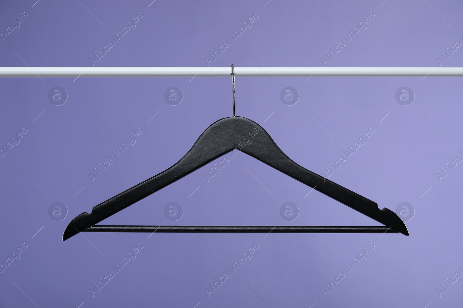 Photo of Black clothes hanger on rack against purple background