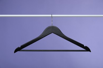 Photo of Black clothes hanger on rack against purple background