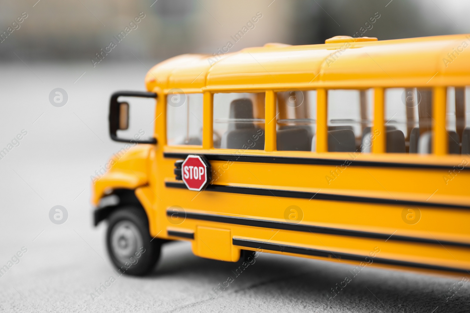 Photo of Yellow toy school bus against blurred background, closeup. Transport for students