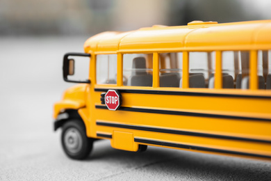 Yellow toy school bus against blurred background, closeup. Transport for students