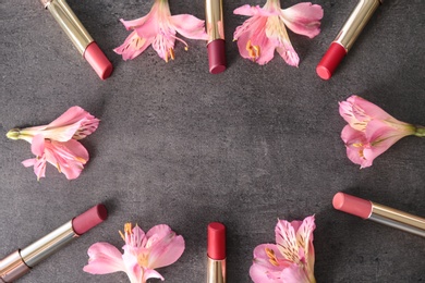 Photo of Frame made with bright lipsticks and spring flowers on grey table, flat lay. Space for text