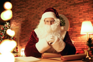 Photo of Santa Claus with wish list at table indoors