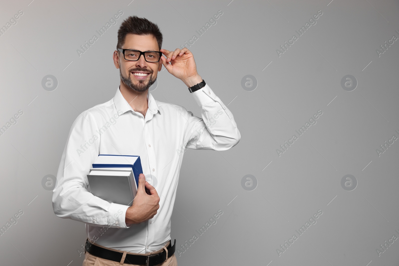 Photo of Happy teacher with glasses and books against beige background. Space for text