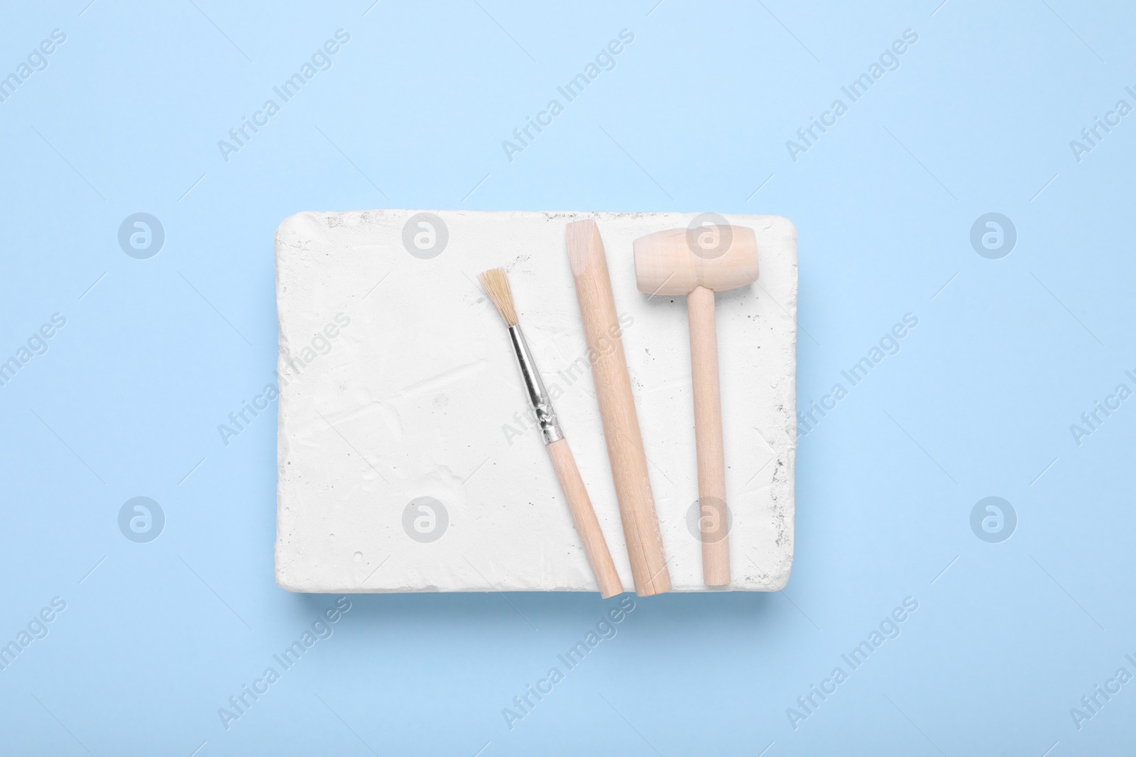 Photo of Educational toy for motor skills development. Excavation kit (plaster, digging tools and brush) on light blue background, top view
