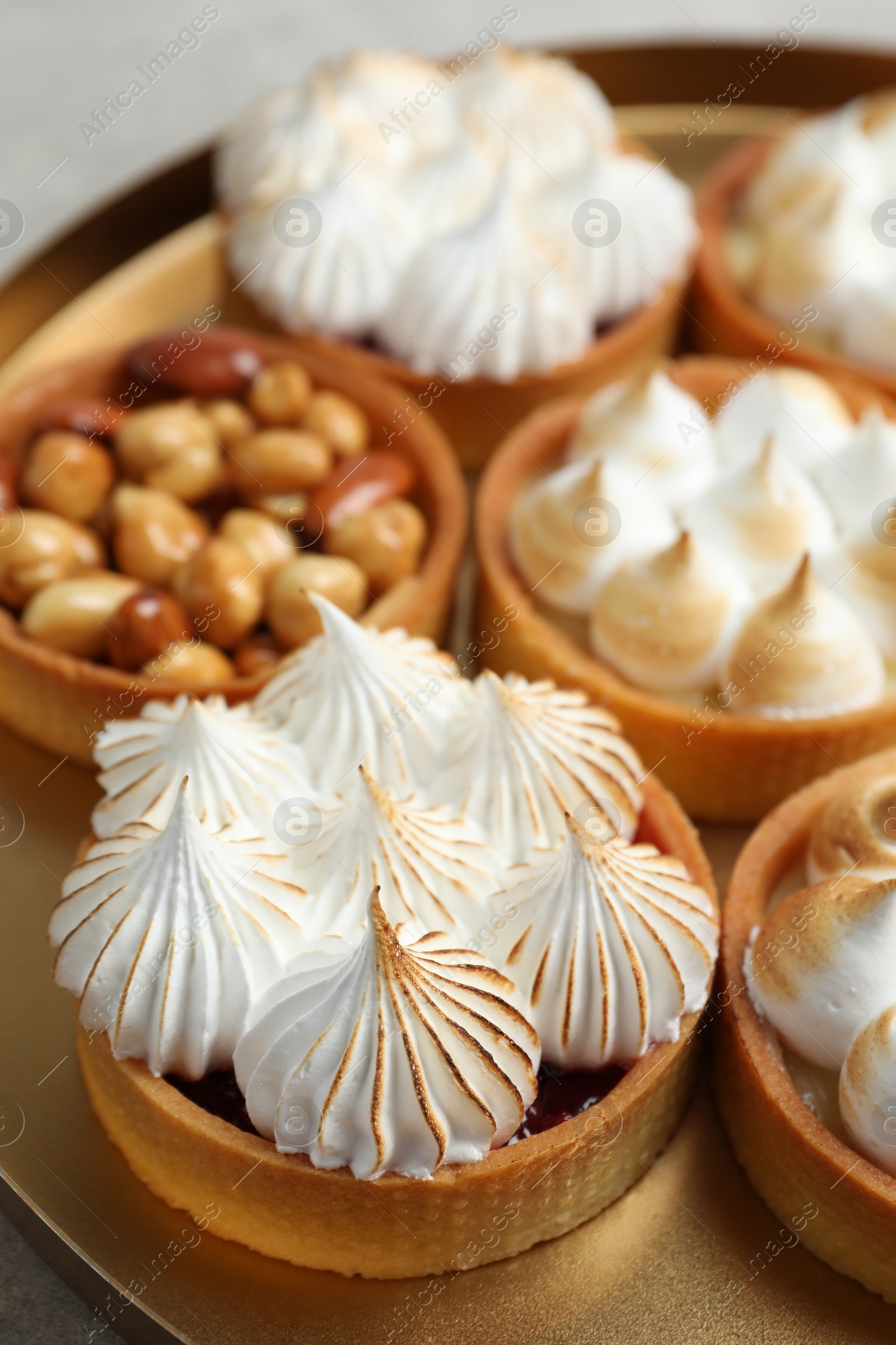 Photo of Many different tartlets on table in golden tray, closeup. Delicious dessert