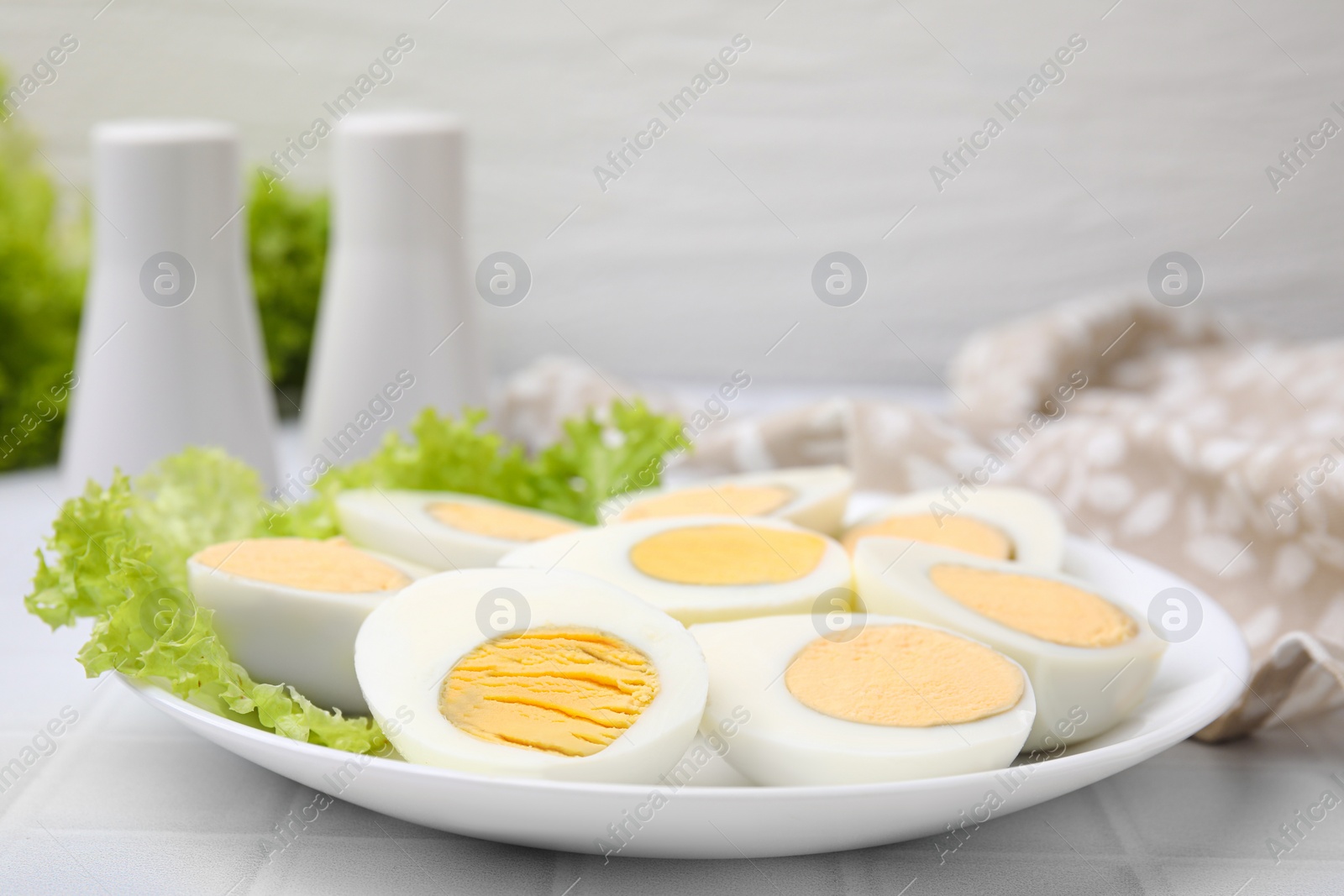 Photo of Fresh hard boiled eggs and lettuce on white tiled table, closeup