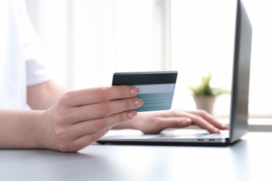 Photo of Online payment. Woman with laptop and credit card at white table, closeup