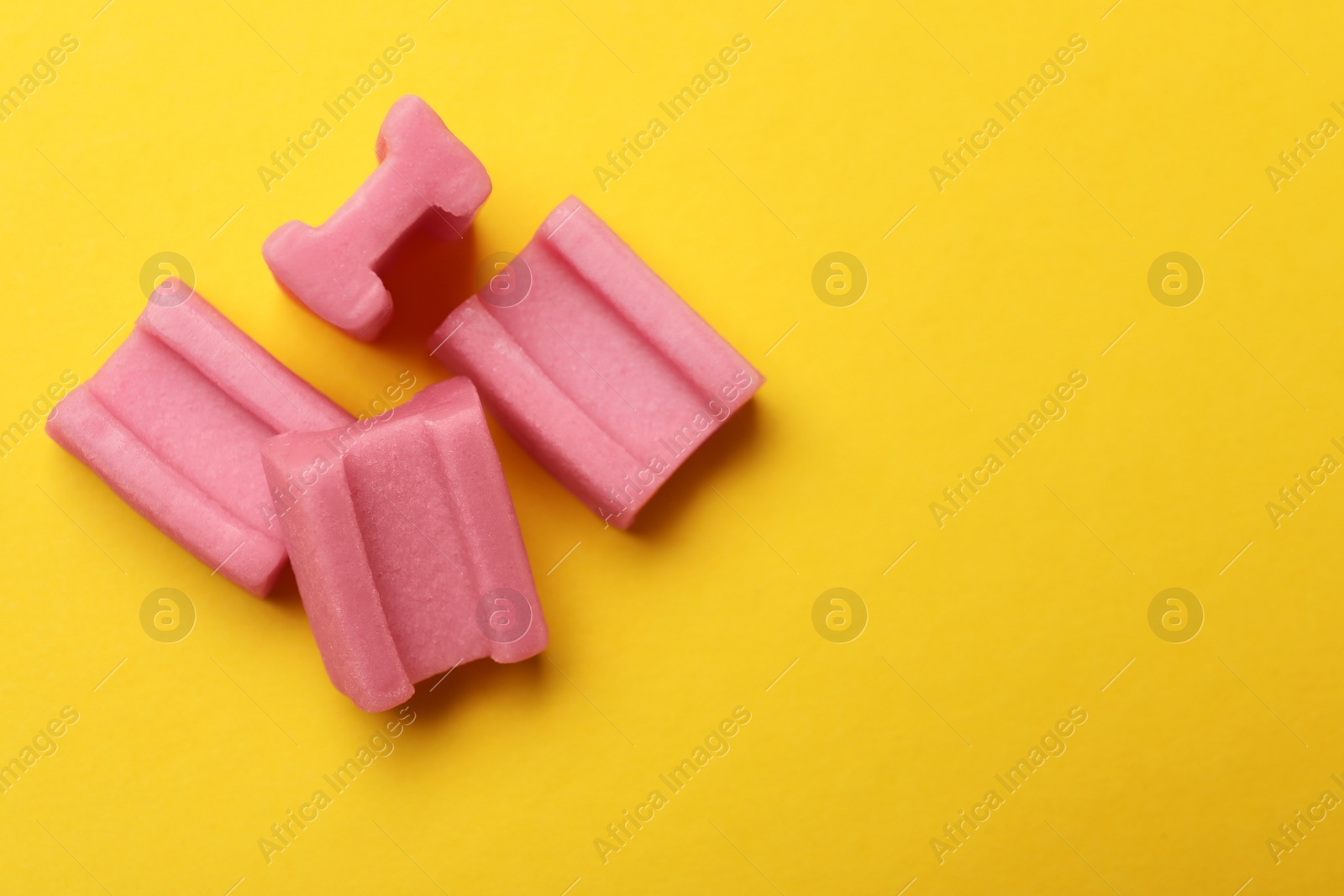 Photo of Tasty pink chewing gums on yellow background, flat lay. Space for text