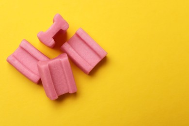 Photo of Tasty pink chewing gums on yellow background, flat lay. Space for text