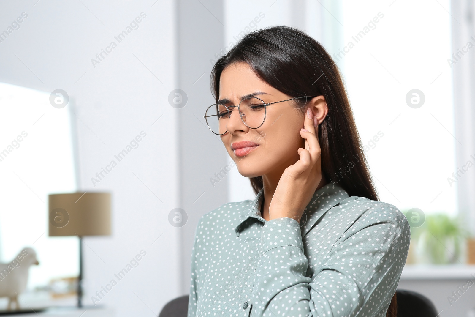 Photo of Young woman in eyeglasses suffering from ear pain indoors